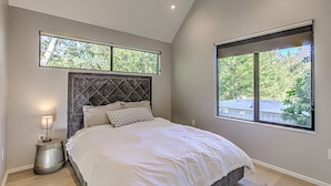 A bedroom with a bed, a nightstand, a window, and a view of trees. - New 2 BDRM Home I Mins to DT Walk to Shops & More (Austin)