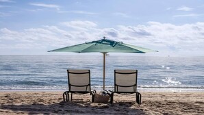 Duas cadeiras de praia sob um guarda-sol, voltadas para o oceano.