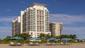 Um hotel moderno com vários sacadões, localização à beira-mar e guarda-sóis na praia.