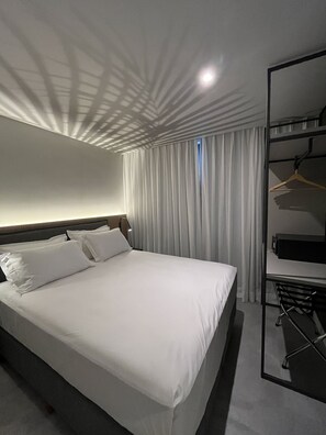 A hotel room with a large bed, a desk, a chair, and a wardrobe. - Boutique Apartment (Itajaí)