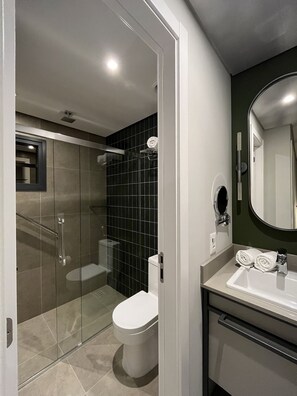 A modern bathroom with a glass-enclosed shower, a white toilet, and a vanity with a mirror. - Boutique Apartment (Itajaí)