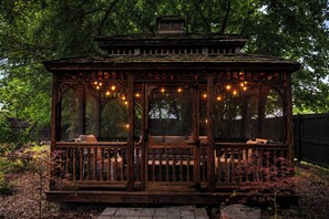A wooden gazebo with a bench and string lights, surrounded by trees. - Private Garden Home w/ Large Fenced Yard + Gazebo (Richmond)