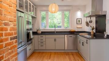 A modern kitchen with a brick wall, stainless steel appliances, and a large window.