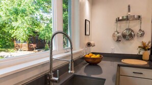 Una cocina moderna con un lavamanos de acero inoxidable, un cuenco de madera con fruta y una ventana con vistas a la vegetación.