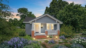 Una casita con porche, rodeada de un jardín lleno de flores.