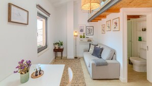 Een moderne woonkamer met een bank, een eettafel en een vloerlamp. Er is een trap die naar een hoger gelegen verdieping leidt.