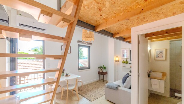 Een modern interieur met een loft-achtige zoldervloer, een eethoek met een tafel en stoelen, een bank en een klein bijzettafeltje met een plant.