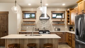 Une cuisine moderne dotée d’un îlot central, de tabourets de bar en bois, d’appareils électroménagers en acier inoxydable et de téléviseurs intégrés.