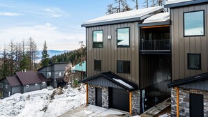 Une maison moderne à plusieurs étages, dotée d’un garage, d’un porche abrité et offrant une vue sur un paysage enneigé.