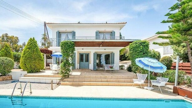 A two-story house with a swimming pool, a covered patio, and a garden with neatly trimmed bushes.
