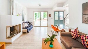 A spacious living room with a fireplace, a sofa, a coffee table with a plant, and a dining area with chairs.