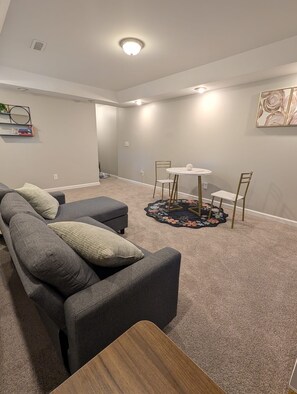 A living room with a gray sectional sofa, a round coffee table, and a small dining table with chairs. - Cozy 3BR 1BA Basement (Conley)