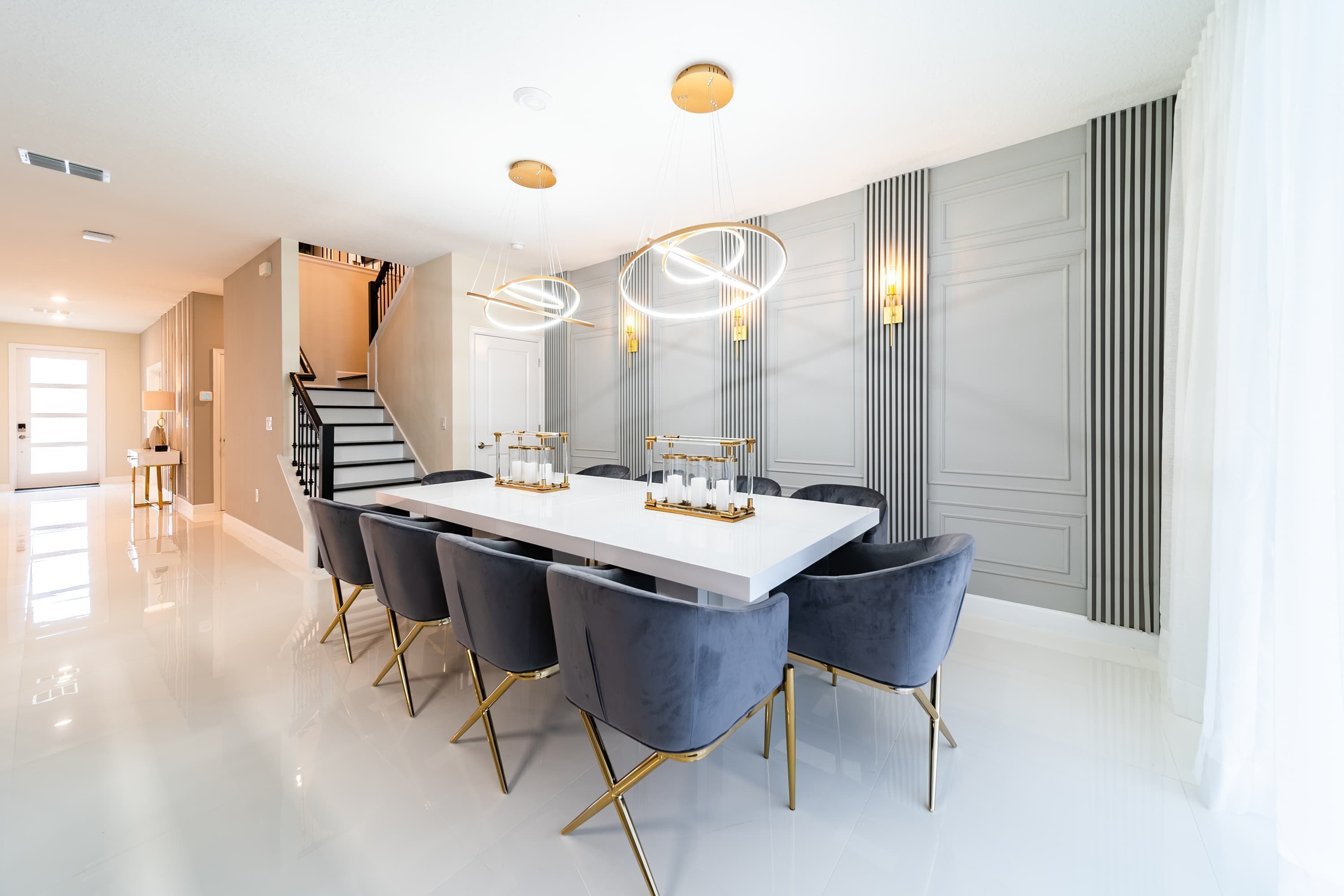 A modern dining area with a white table, dark chairs, and a staircase in the background.