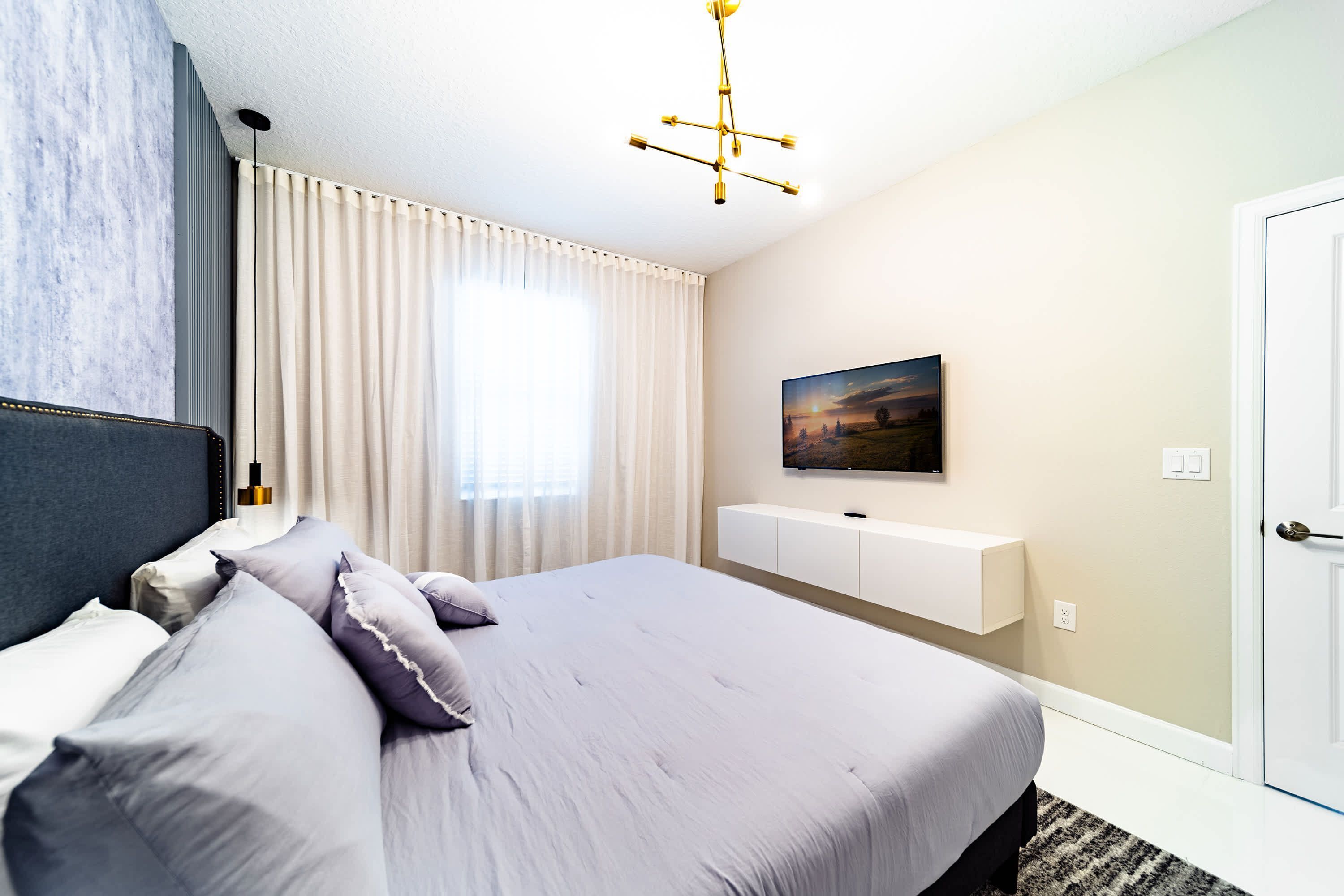Un dormitorio moderno con una cama grande, un televisor montado y un cuadro en la pared.