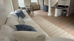 Ett rymligt vardagsrum med en stor beige soffa, en matplats och en trappa som leder upp till ett övre plan.