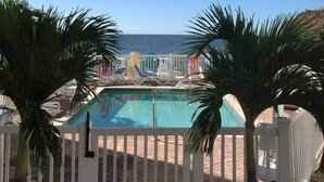 A pool area with a view of the sea, surrounded by palm trees and a white fence. - 102 - Newly renovated house Oceanside  and Pool (Cudjoe Key)
