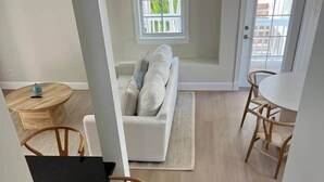 A modern living room with a white sofa, wooden chairs, a round wooden table, and a window with blinds. - 102 - Newly renovated house Oceanside  and Pool (Cudjoe Key)
