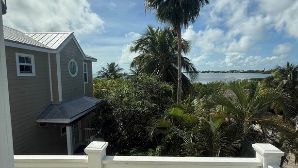 A wooden deck with a white railing, a house with a grey roof, and a tall palm tree in the background. - 105 - Newly renovated house Oceanside  and Pool (Cudjoe Key)
