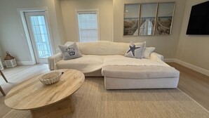 A living room with a sectional sofa, a round wooden coffee table, and a large window with blinds. - 105 - Newly renovated house Oceanside  and Pool (Cudjoe Key)