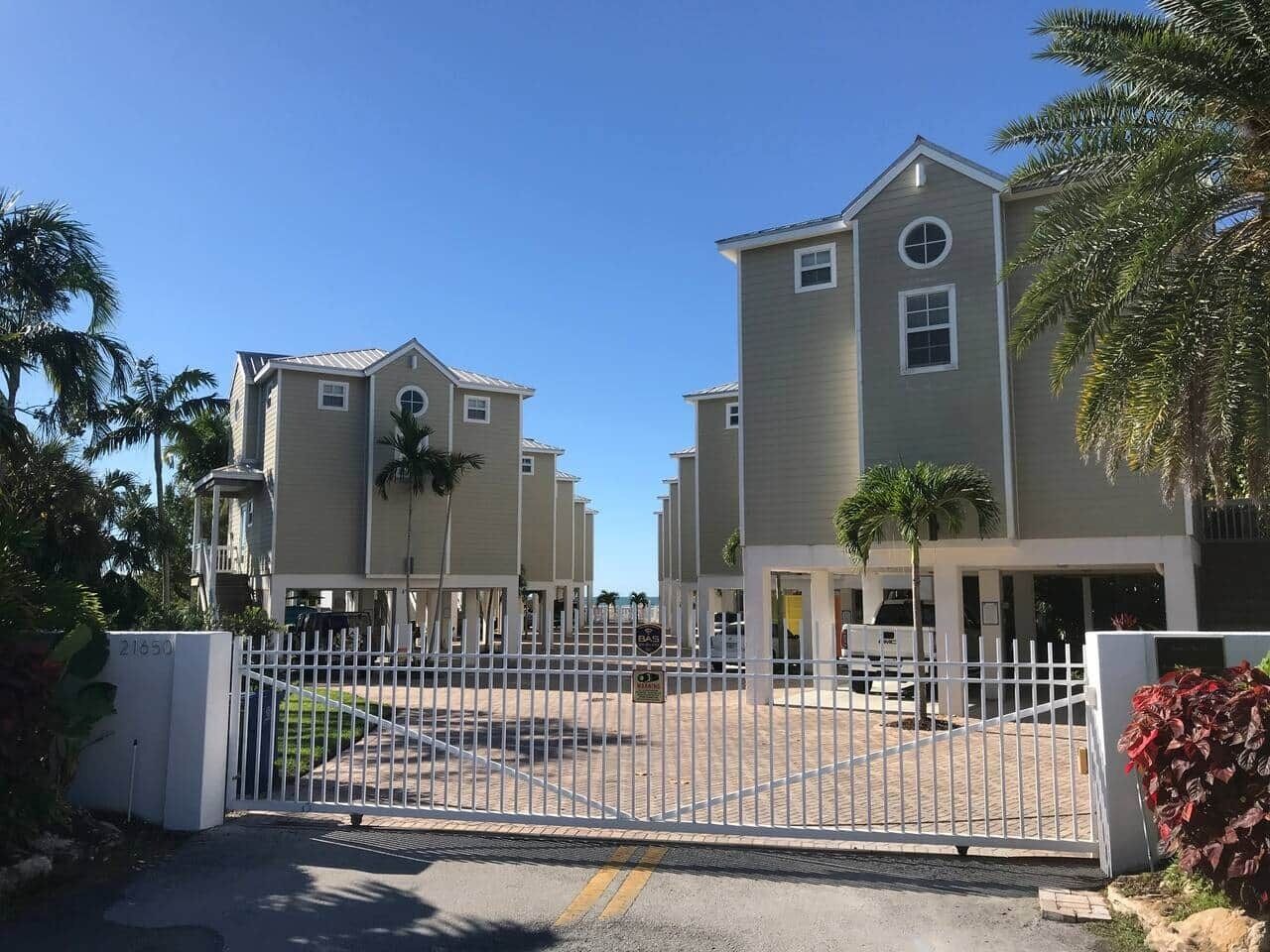 A gated residential complex with multiple two-story houses, a central driveway, and palm trees.