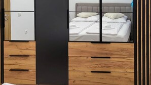 Ein Schlafzimmer mit einem Bett, Holzkasten, einer schwarzen Platte und einem Spiegel, der ein Bett mit Kissen und Kopfteil reflektiert.