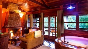 Een gezellig chaletinterieur met een stenen openhaard, een comfortabele bank, een groot raam met uitzicht op groen, en een bad.