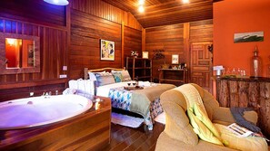 A cozy room with a large wooden bed, a sitting area with a sofa, and a wooden wall with a large mirror and artwork. - Pousada Verde Água Visconde de Mauá (Itatiaia)