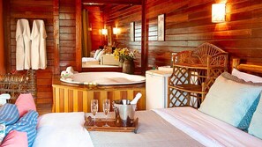 A wooden cabin-style room with a bed, a wooden chair, a small table with a tray, a bucket, and a hot tub. - Pousada Verde Água Visconde de Mauá (Itatiaia)