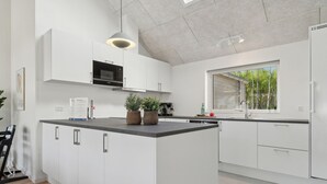 Cozinha moderna com armários brancos, uma ilha central, micro-ondas e uma janela com vista para vegetação.