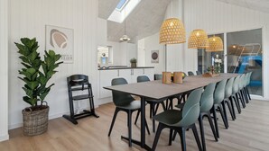Uma sala de jantar moderna com uma mesa comprida, várias cadeiras e luminárias pendentes.