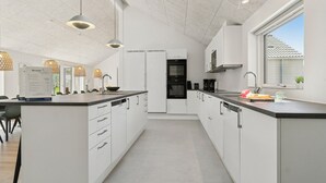Ett modernt kök med vita skåp, en stor köksö och hängande lampor.