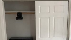 Een kamer met een witte deur, een donker houten dressoir en een kapstok met een zwart jas.