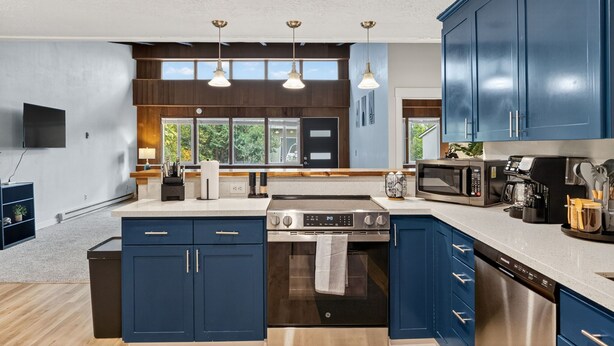 A modern kitchen with dark blue cabinets, stainless steel appliances, and pendant lighting. - Mid-Century Escape, Near Forest Park (Portland)