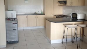 Een keuken met lichte houten kastjes, een wit aanrecht, een inbouwmagnetron, een gasfornuis en een wasmachine.