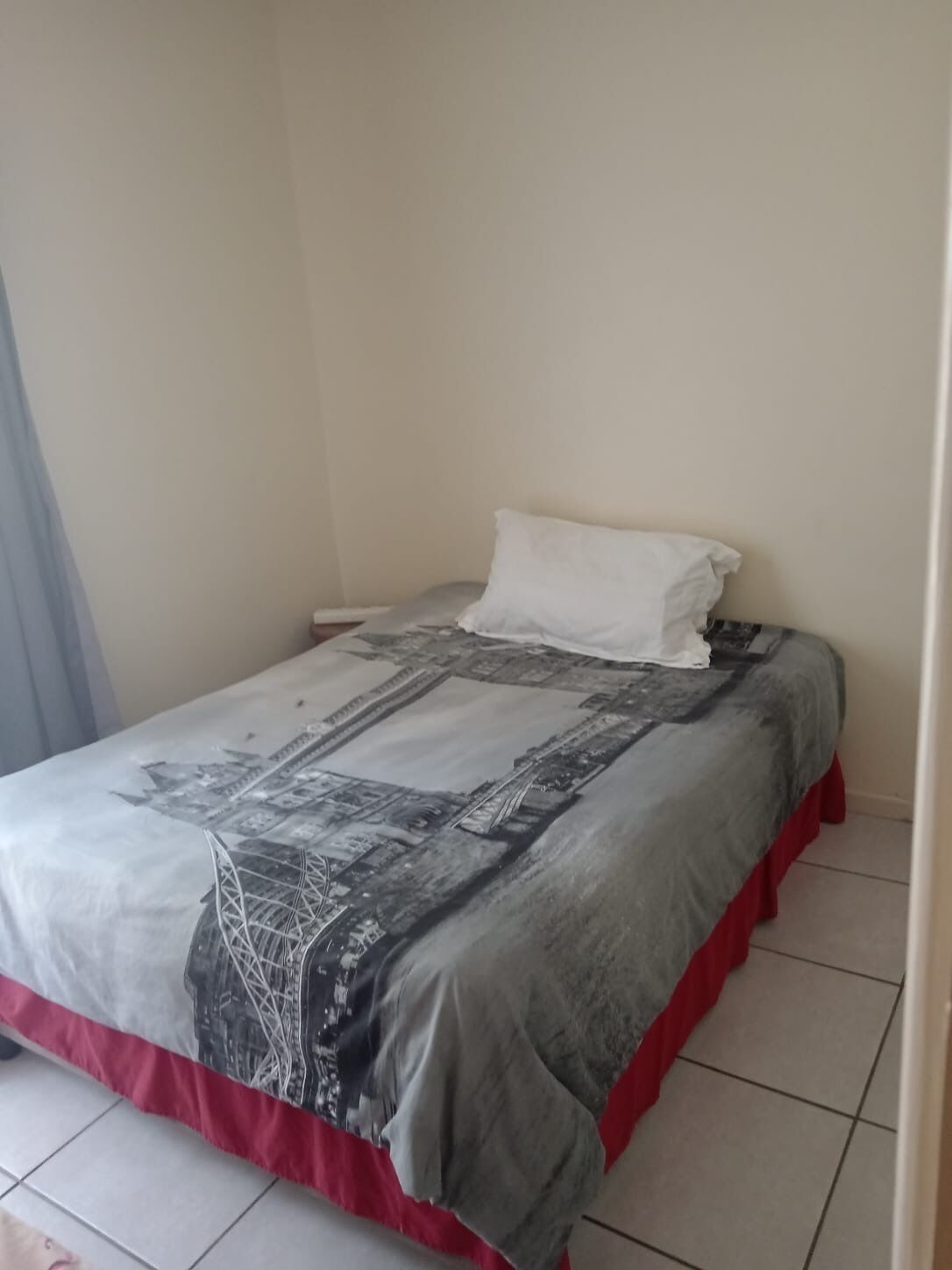 Un lit avec une couvre-lit à motifs, un oreiller blanc et un pied de lit rouge.