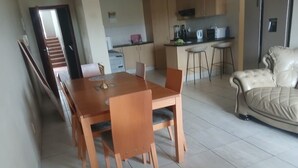 Een eetgedeelte met een houten tafel en stoelen, een bank en een keuken op de achtergrond.