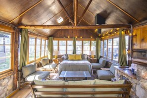 Una cabaña con interior de madera, una cama, zona de estar y ventanas amplias.
