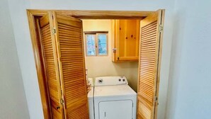 Un lavadero con lavadora, armarios de madera y ventana.