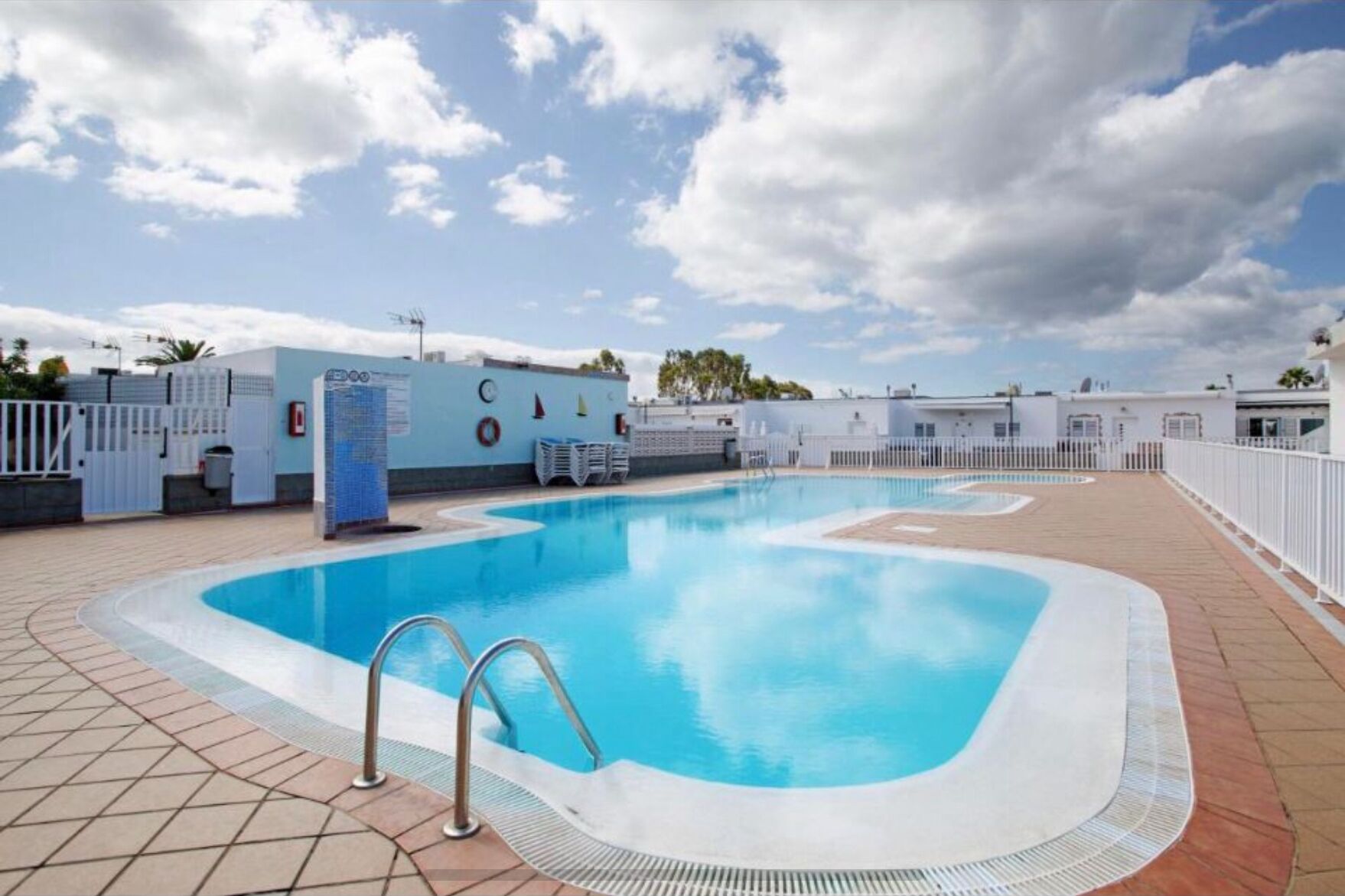 En swimmingpool med ett kaklat poolområde, en livräddarstation och ett vitt staket som omger området.