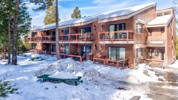 Una cabaña de madera de varios pisos con balcones, rodeada de nieve y árboles.