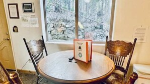 A round table with a book on it, surrounded by wooden chairs, in a room with a window overlooking a rocky outdoor area. - Yosemite Woods Lower Unit - Inside Yosemite (Yosemite West)