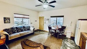 A living room with a sofa, a dining table with chairs, a ceiling fan, and a kitchen area with a refrigerator. - Yosemite Woods Lower Unit - Inside Yosemite (Yosemite West)