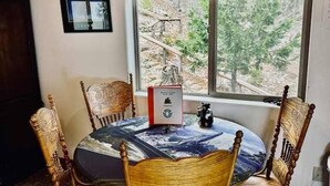 Una mesa redonda de comedor con mantel estampado, rodeada por cuatro sillas de madera. Un cuadro enmarco cuelga de la pared sobre la mesa, y un pequeño adorno se encuentra sobre la mesa.