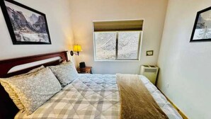 Un dormitorio con cama, ventana, mesita de noche y lámpara.