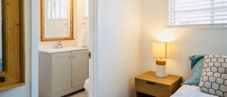 Ein Schlafzimmer mit Bett, Nachttisch mit Lampe, Waschbecken und Bad mit Spiegel.