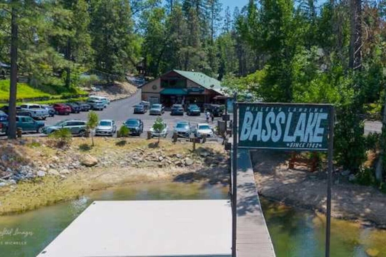 A sign for Bass Lake with a parking lot and a building in the background.