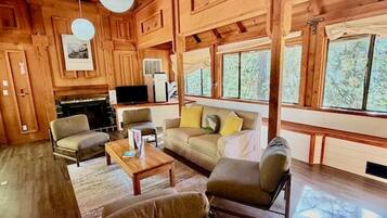 A cozy cabin interior with a fireplace, wooden walls, and large windows.