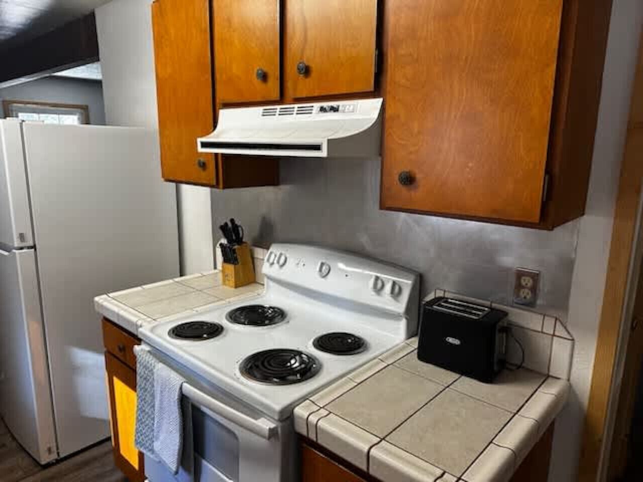 A compact kitchen with a white stove, wooden cabinets, and a toaster.
