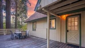 A wooden deck with a table and chairs, a door with a window, and a view of trees.