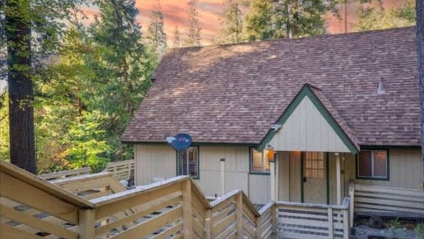 A cabin with a wooden deck, a porch, and a mountain backdrop.
